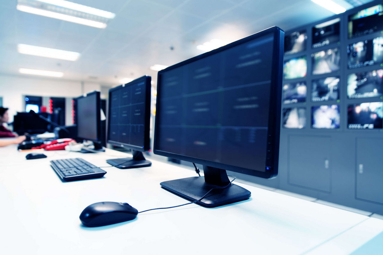 System Security Specialist Working at System Control Center. Room is Full of Screens Displaying Various Information.