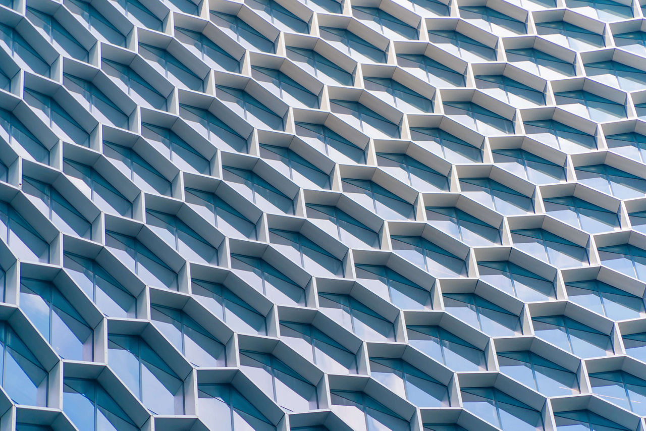 Office buildings. Structure of hexagon windows in futuristic technology network connection concept. Blue glass modern architecture facade design with reflection of sky in urban city, Downtown.