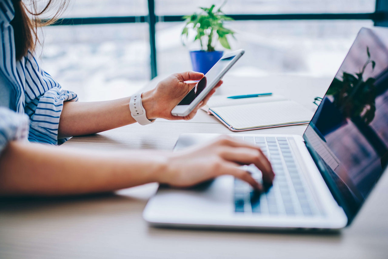 Cropped image of female holding smartphone getting message with confirmation making transaction on laptop computer,woman using mobile phone app for synchronizing data with netbook via bluetooth.