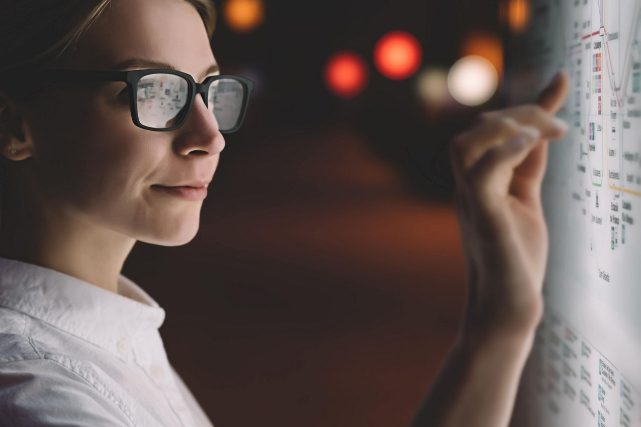 公共地下鉄マップのデジタルモニター。高度な革新的技術を使用した大画面のそばに立っている女性。若い女性が高感度スクリーンを指で触り、画面のオプションを選択している