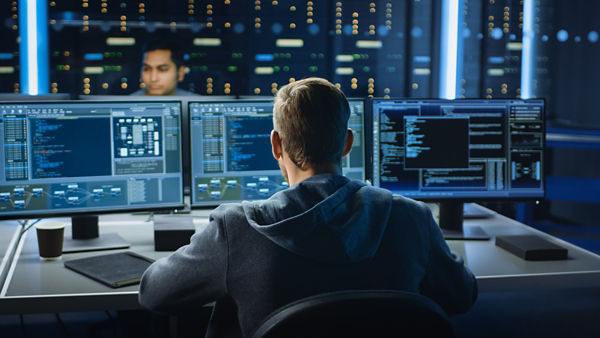 Two IT professionals working a dark office monitoring multiple monitor screens