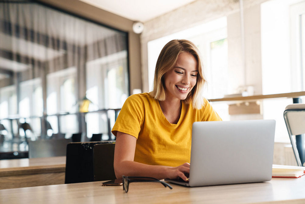 Photo of joyful nice woman using laptop and smiling while sitting