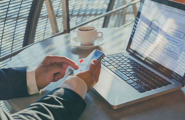 hands holding a smart phone in front a laptop using two-factor authentication