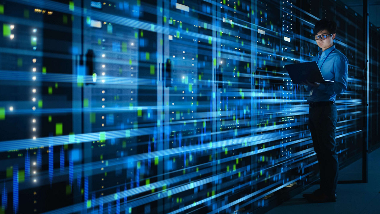 Profesional de redes de pie, sosteniendo una computadora portátil abierta en una sala de centro de datos oscura