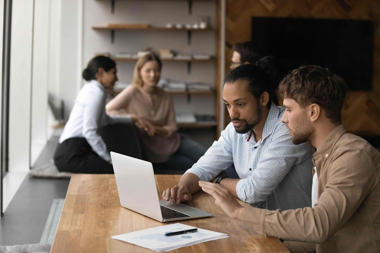 Two diverse male employees working on project together using laptop
