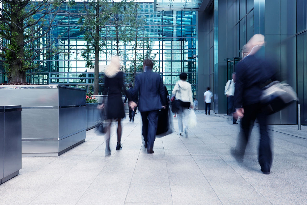 Blurred image of business professionals walking through a modern office plaza with glass walls