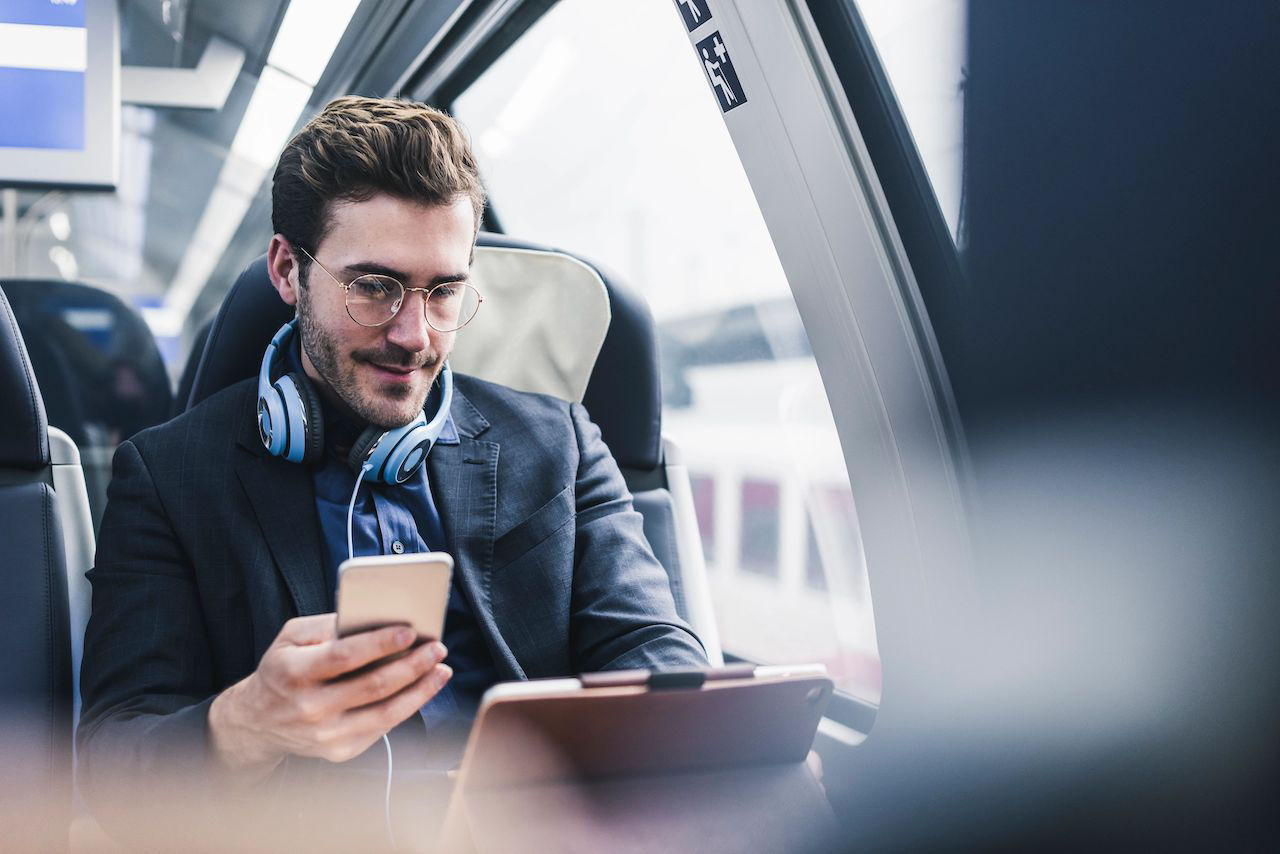 Network professional sitting in train with cell phone, headphones and tablet