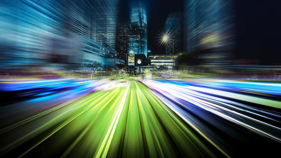 前面へと流れる緑、青、白色の明るいライトが速い動きを示すぼやけた街並み