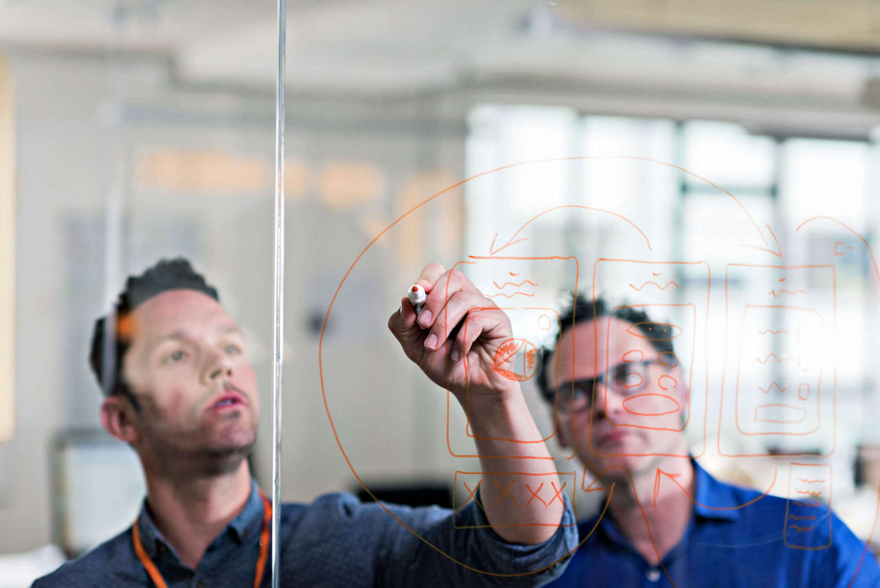 Two developers writing on a glass wall with orange marker.