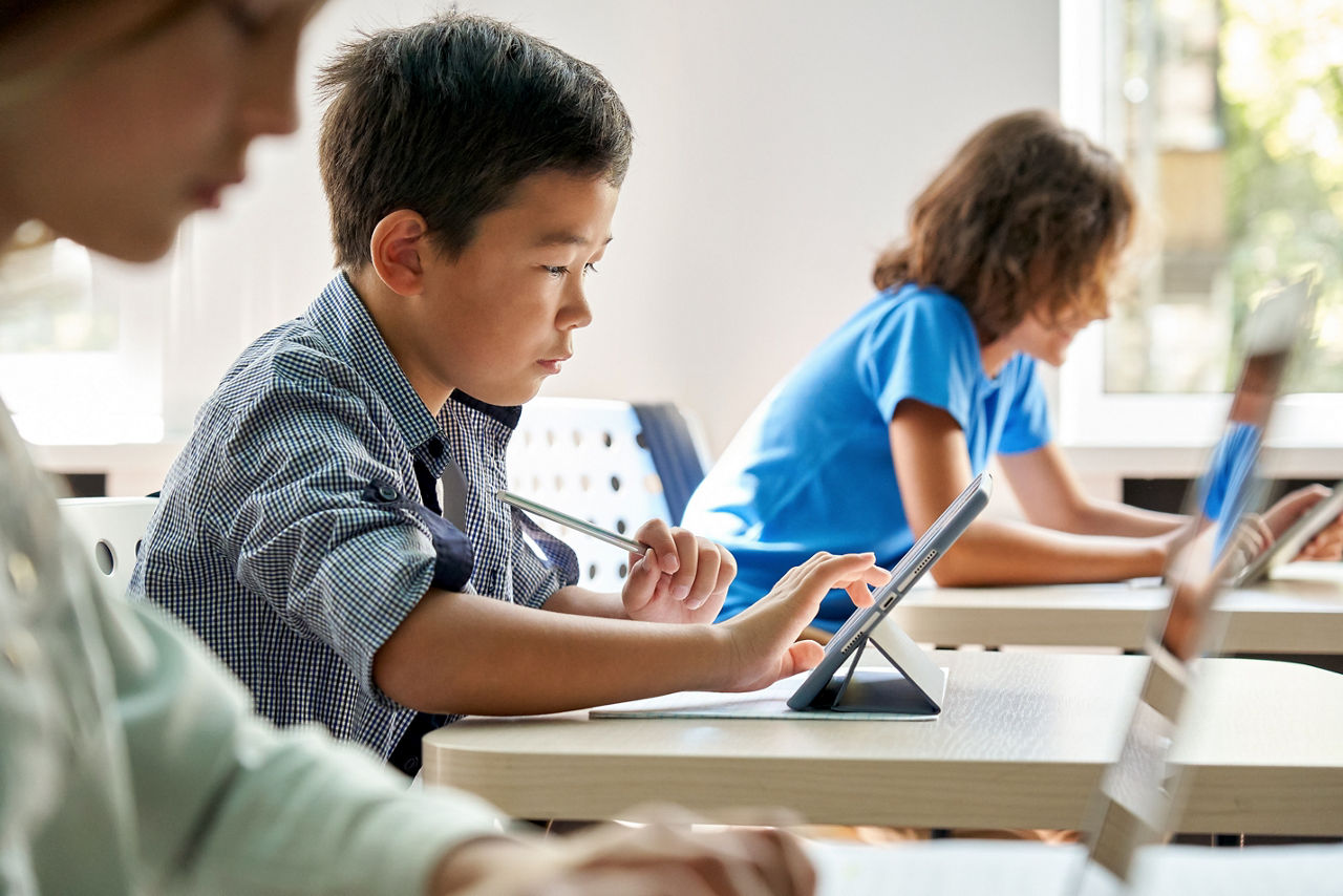 Focused Asian school boy using digital tablet at class in classroom.