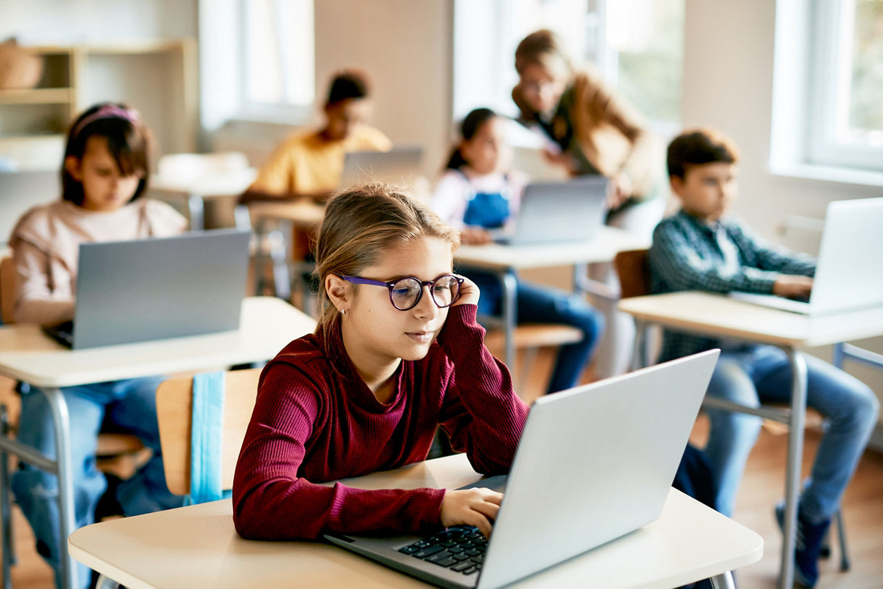 Little girl e-learns on laptop in computer science classroom at elementary school.
