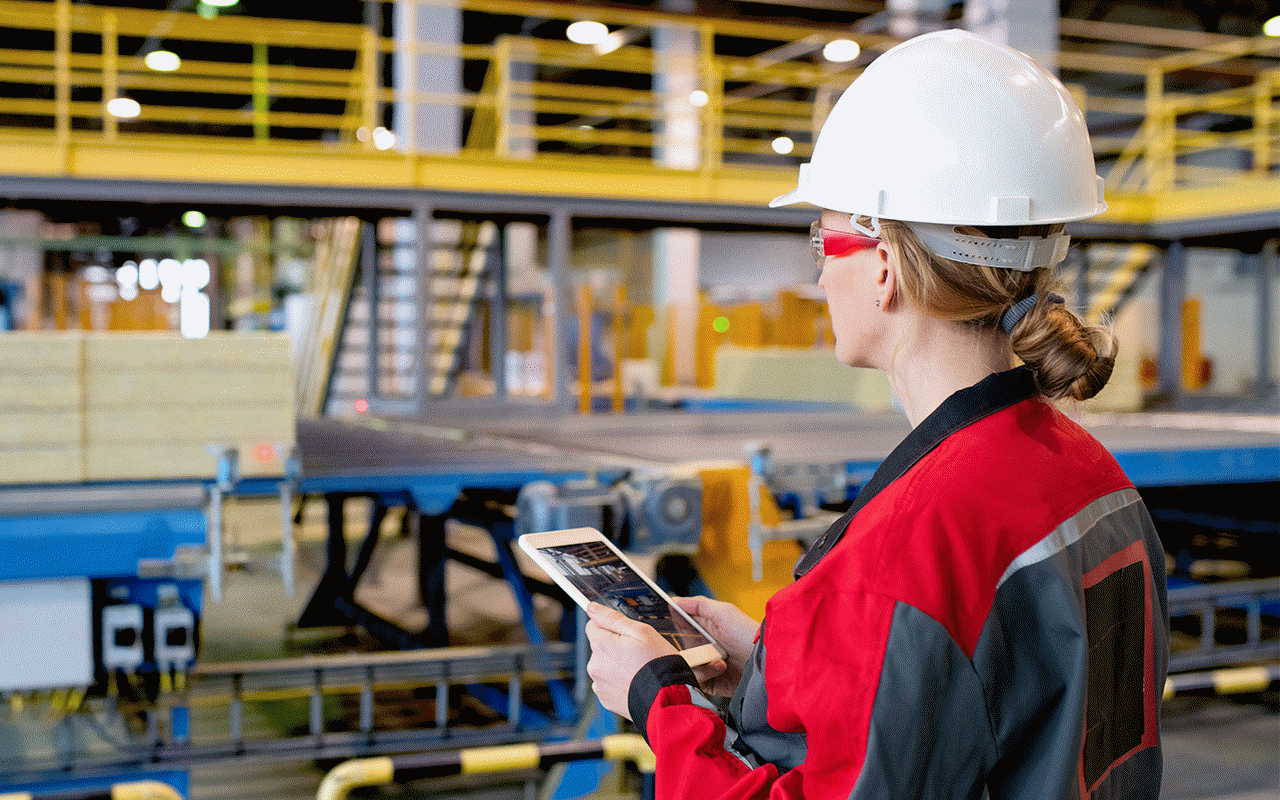製造ファシリティ内でヘルメットをかぶり、モバイルデバイスを持っている作業者