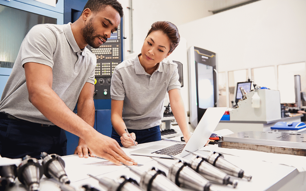 製造ファシリティのワークスペースで、ラップトップの前で協力する同僚たち